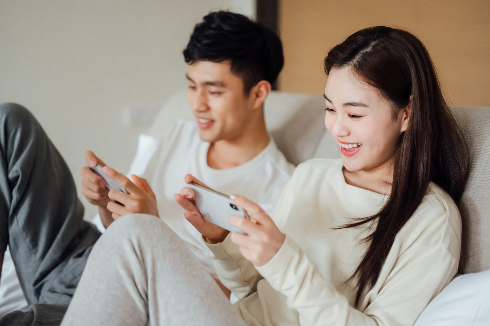 Young couple playing online games with smartphone in bedroom